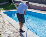 Man cleaning the pool at home, standing with the cleaner device, doing chores, housework, household