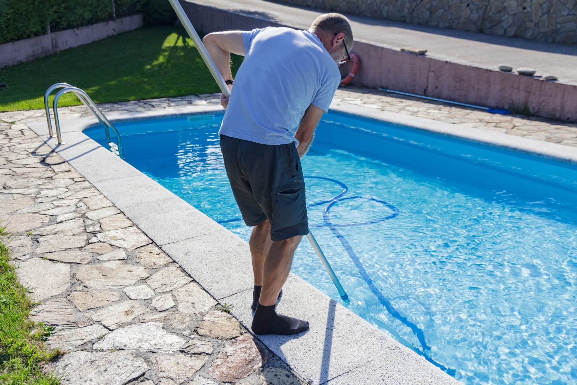 Man cleaning the pool at home, standing with the cleaner device, doing chores, housework, household
