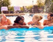 Smiling Family With Mature Parents And Adult Offspring On Summer Holiday In Swimming Pool On Airbed